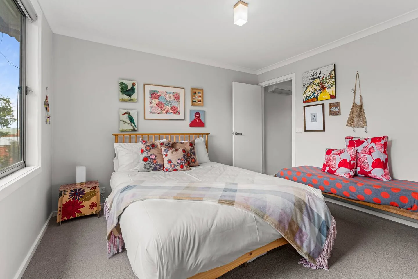 Un dormitorio con una cama, cuadros coloridos y una ventana.