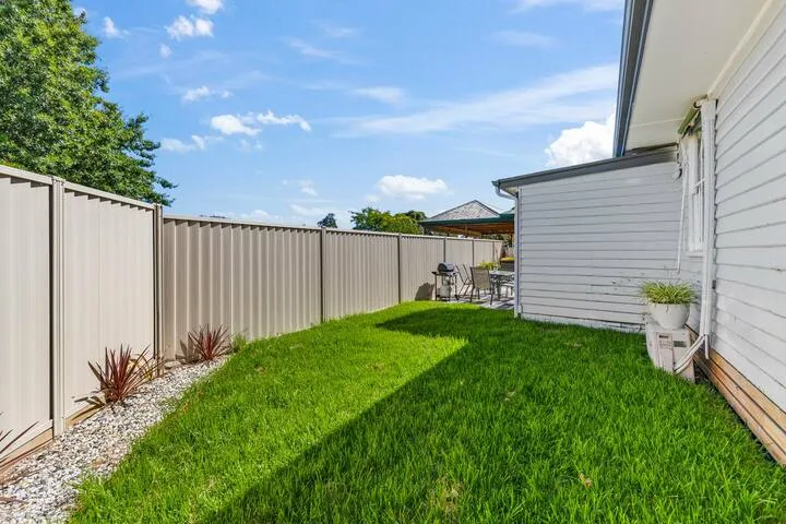 A grassy outdoor area beside a white-sided house and fence.
