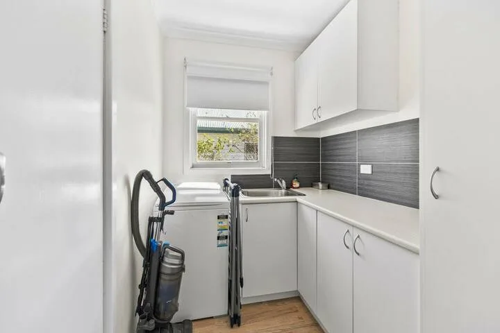 A compact kitchen with white cabinets, a gray backsplash, and a window.