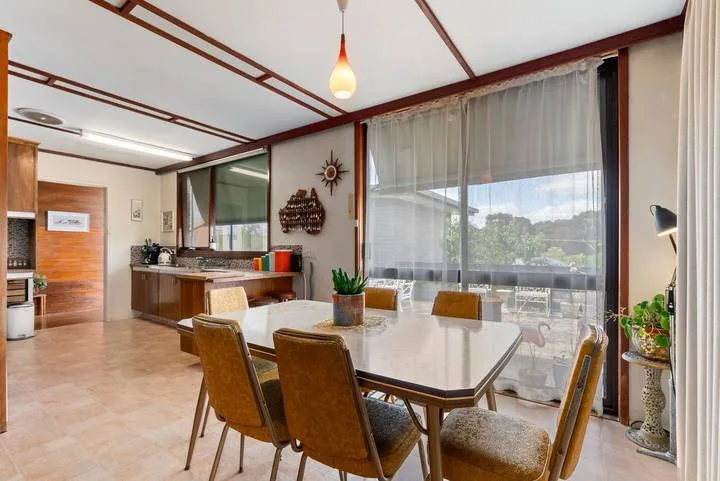 A dining area with a table and chairs beside large curtained windows.