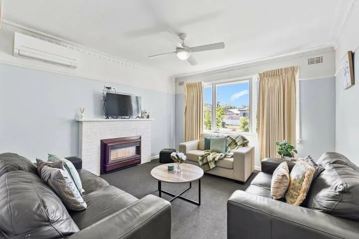 A bright living room with gray seating and a fireplace beside a curtained window.