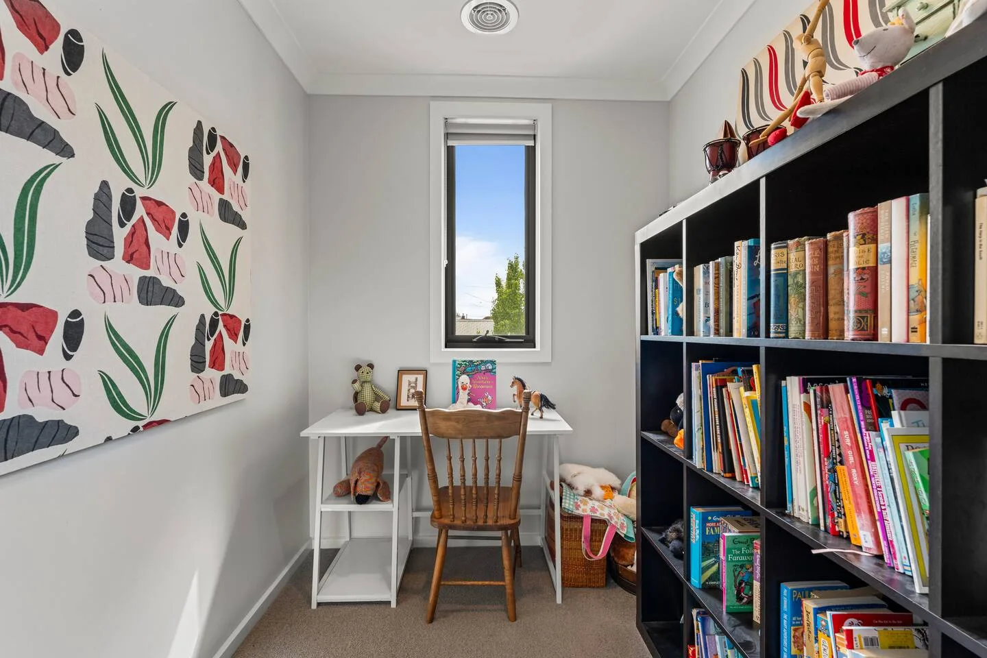 Una zona de estudio tiene un escritorio y una silla bajo una ventana, con estanterías de libros junto a la pared.