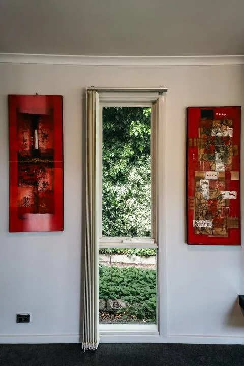 A bright interior room with a narrow window overlooking leafy greenery and red wall art.