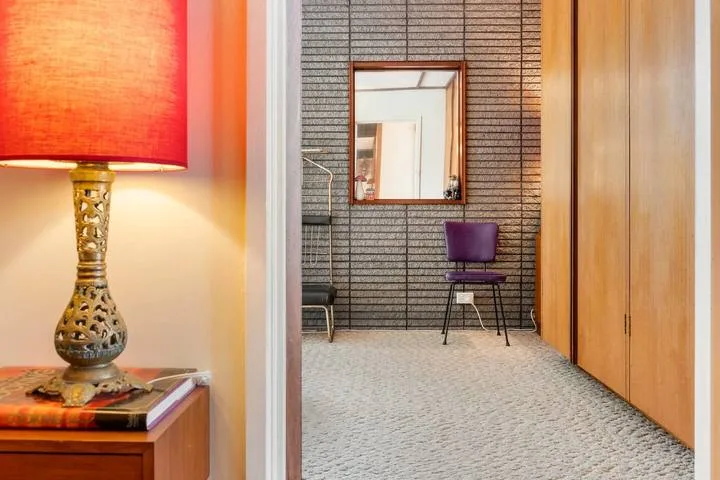 A hallway with a wall mirror and a purple chair beside wooden cabinets.