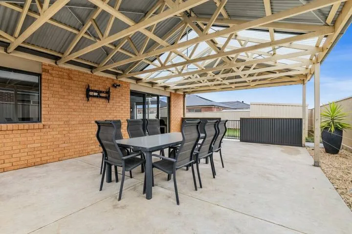 A covered outdoor dining area with a table and seating beside a brick wall.