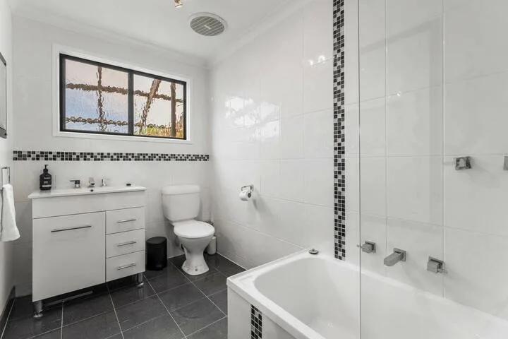 A bright bathroom with a vanity, toilet, and bathtub behind a glass screen.