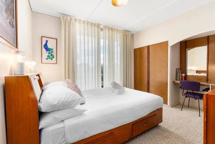 A bedroom with a bed, curtained window, and wooden wardrobe.