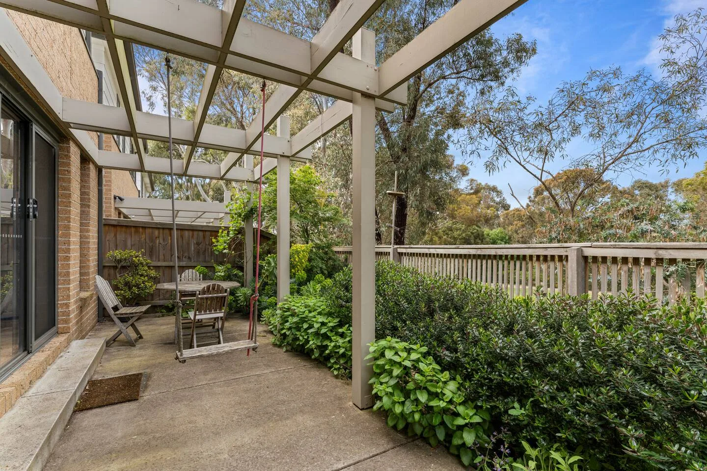 A covered patio with a hanging swing, outdoor seating, and surrounding greenery.