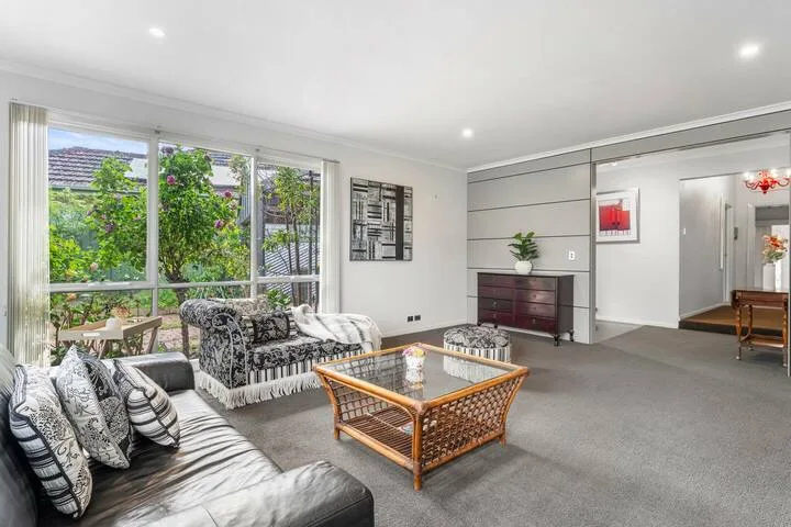 A bright living room with patterned seating and a glass-topped coffee table.