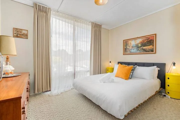 A bedroom with a neatly made bed and a large curtained window.
