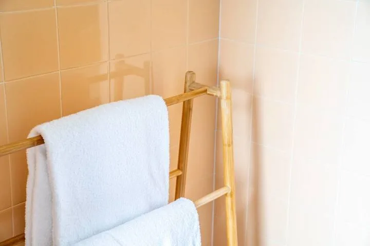 A bathroom with white towels hanging on a wooden rack against tiled walls.