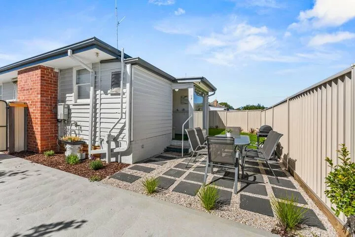 A paved outdoor patio with a table and seating beside a small house.