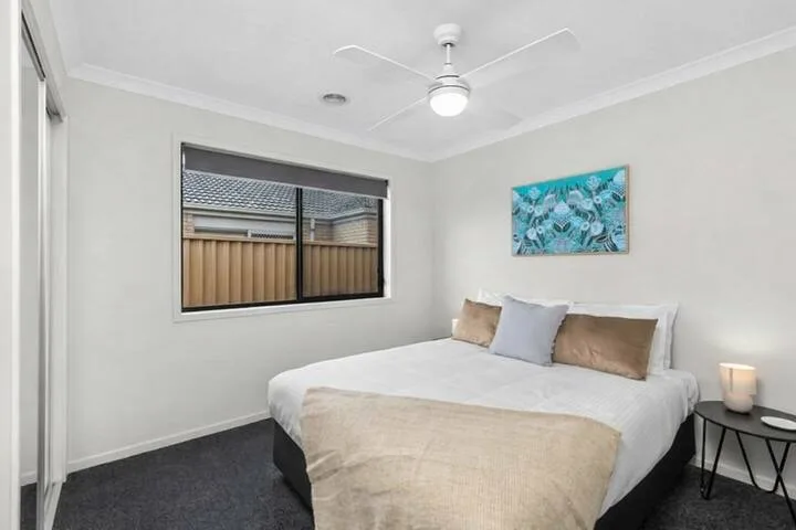 A bedroom with a neatly made bed beneath a ceiling fan.