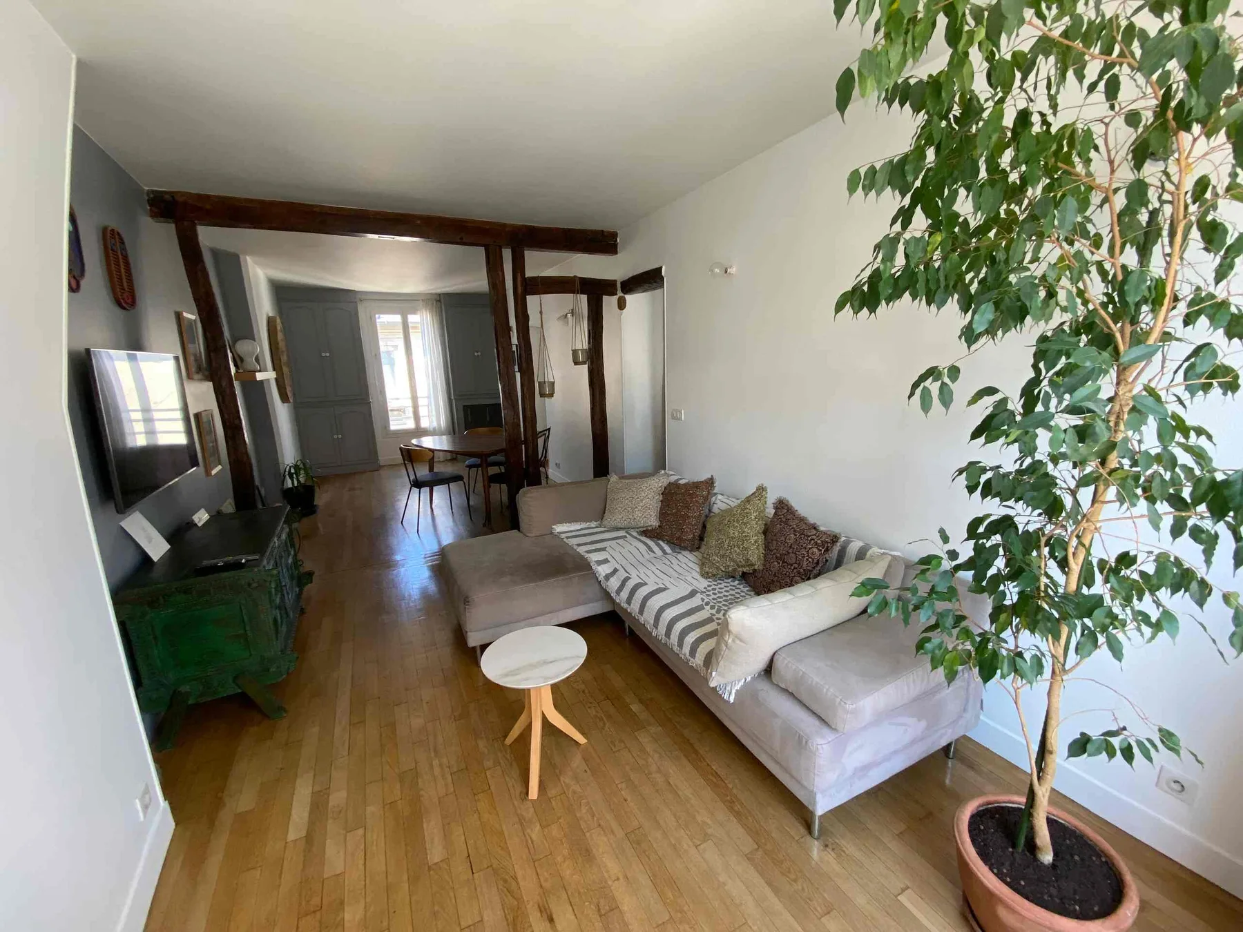 A living room with a sectional sofa, coffee table, and potted tree.