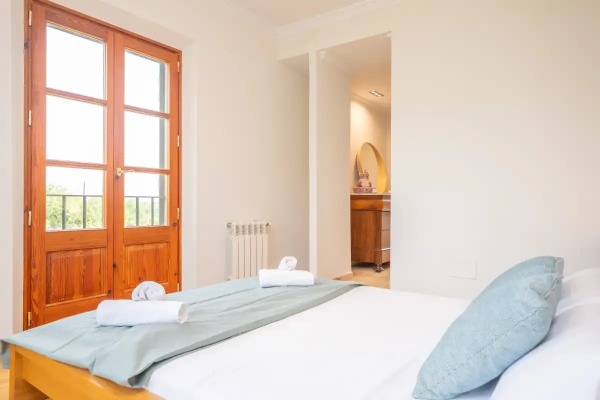 Un dormitorio luminoso con una cama junto a puertas acristaladas con marco de madera.