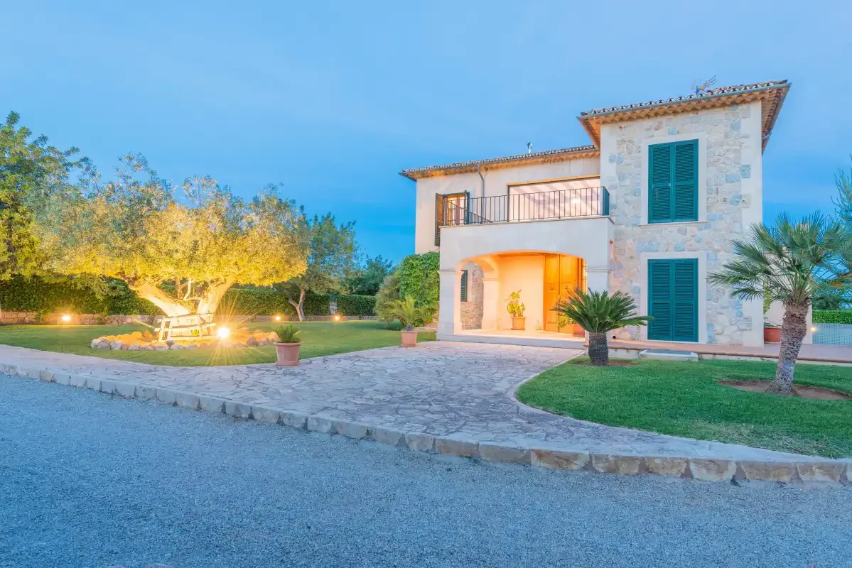 Una casa de piedra se encuentra junto a una entrada pavimentada y un césped ajardinado.