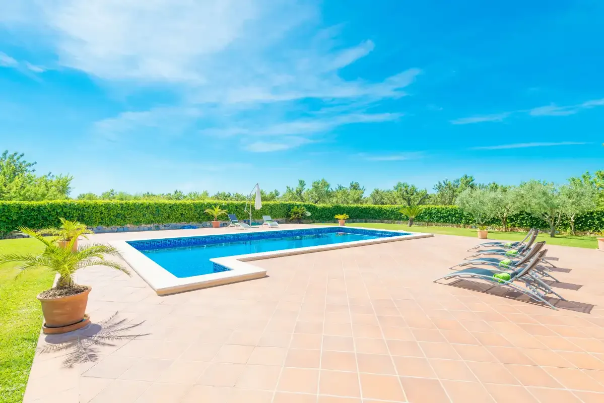 Una piscina al aire libre está rodeada por un amplio patio pavimentado y asientos para descansar.