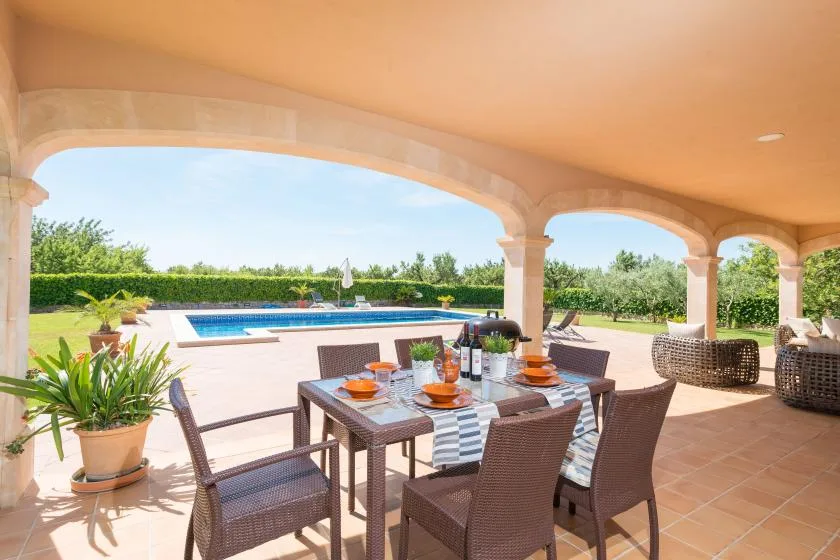 Un patio cubierto con comedor exterior da a una piscina y un jardín.