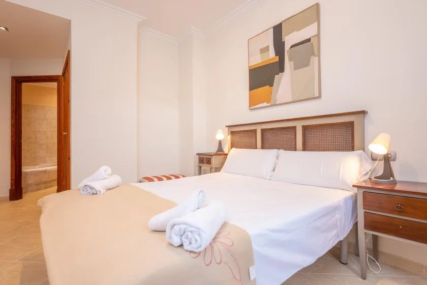 Un dormitorio con una cama tendida, toallas dobladas y arte abstracto en la pared.