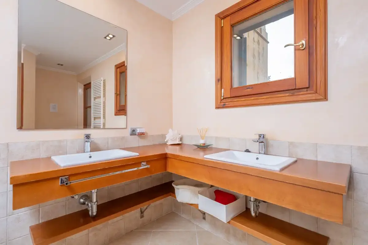 Un lavabo de baño con dos lavabos, un espejo grande y una ventana con marco de madera.