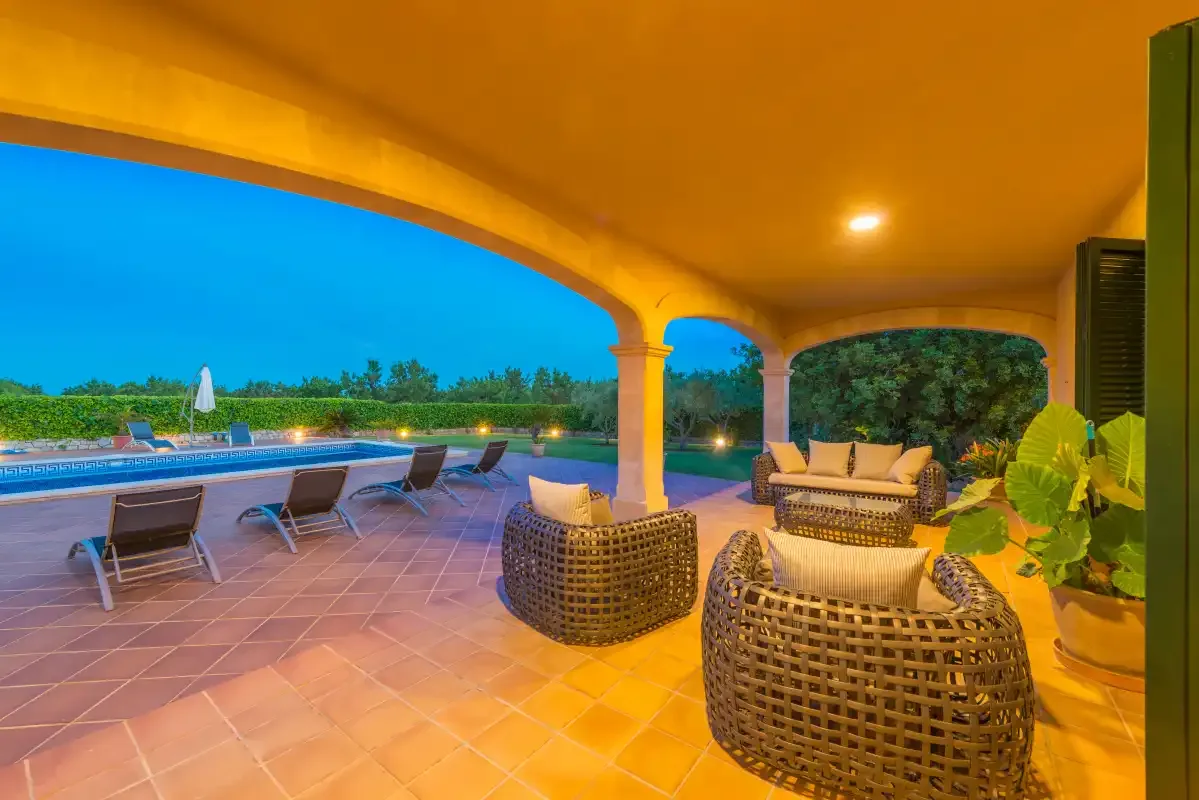 Un patio cubierto con asientos de mimbre da a una piscina.