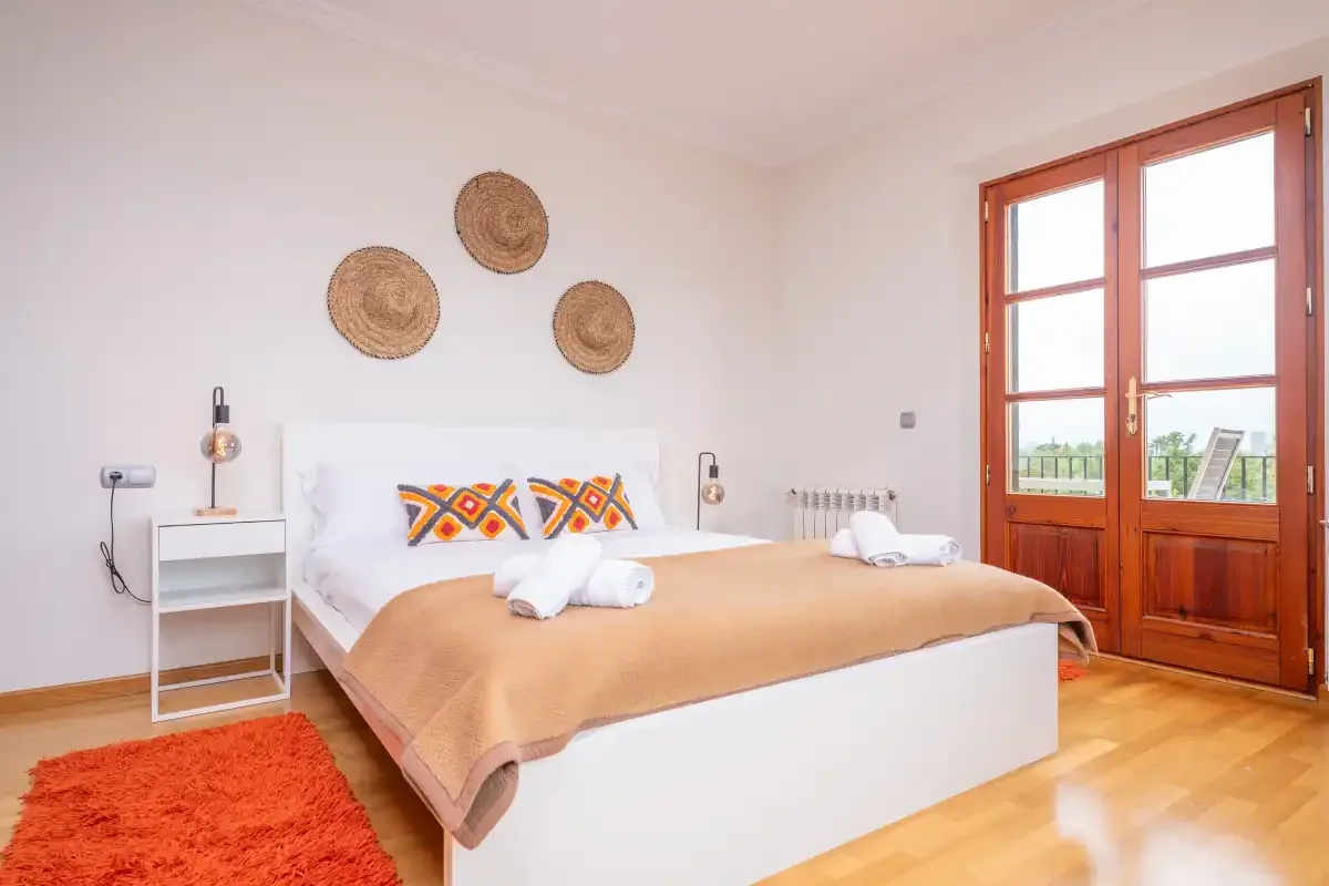 Un dormitorio luminoso con una cama hecha y puertas acristaladas con marco de madera.