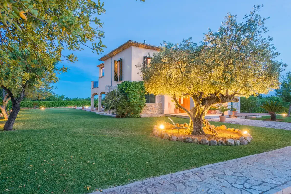 Una casa de dos plantas se encuentra junto a un césped y un árbol iluminado.