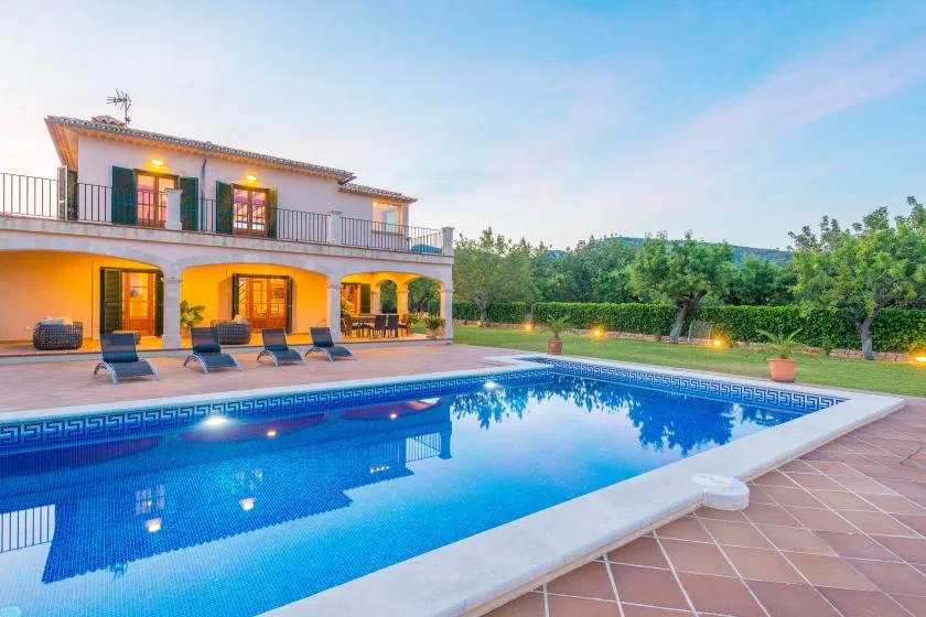 Una piscina junto a una casa de dos plantas y un patio de baldosas.