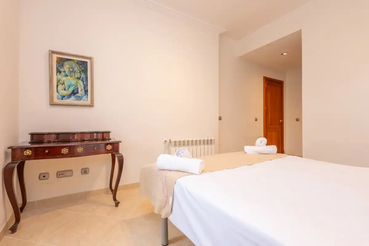 Un dormitorio con una cama hecha, una consola de madera y una obra enmarcada.