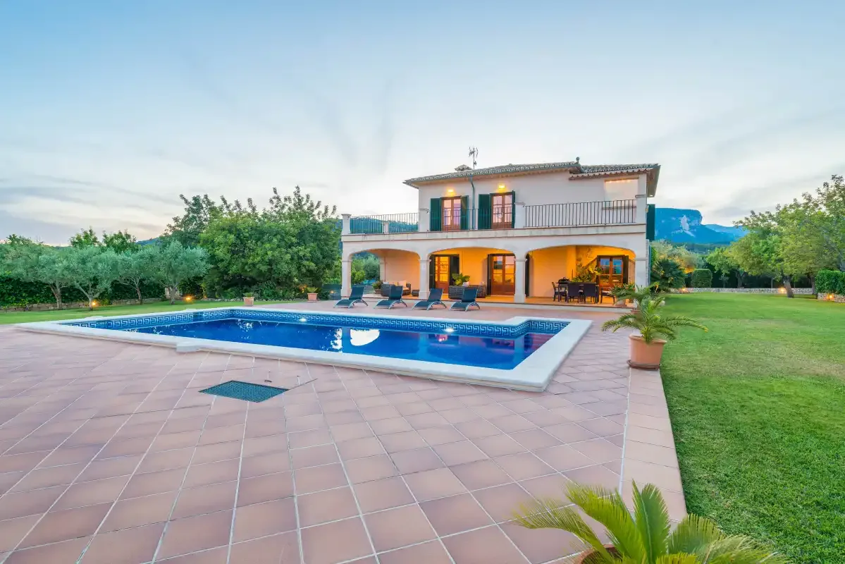 Una casa de dos plantas da a una piscina y un patio pavimentado.