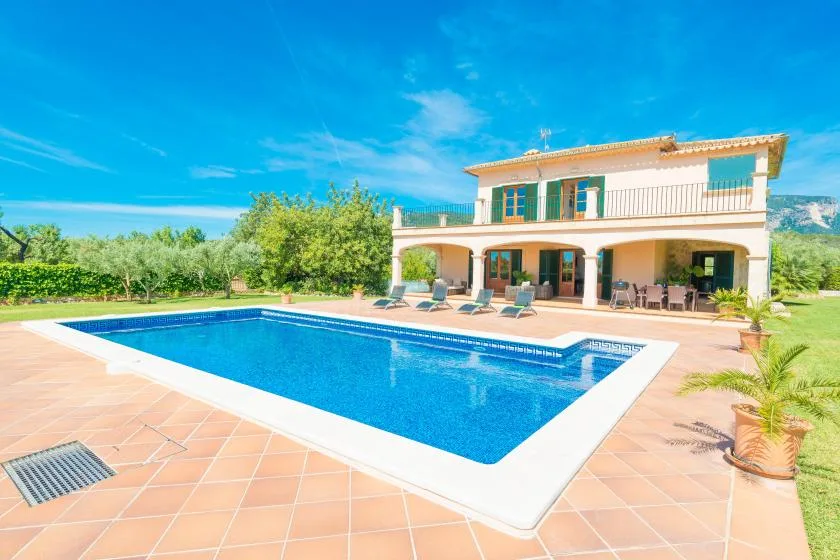 Una piscina y un patio de baldosas están frente a una casa de dos plantas.