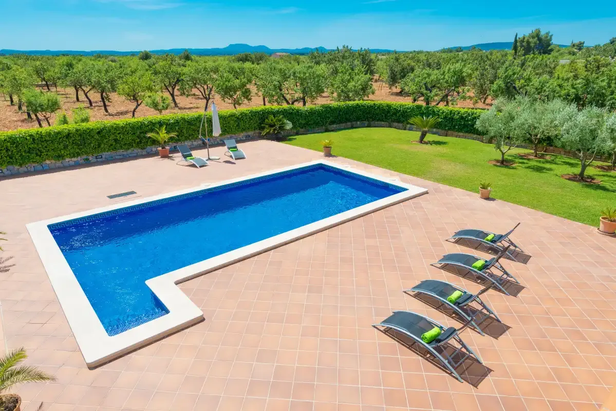 Una piscina al aire libre y un patio de baldosas dan a un huerto verde.