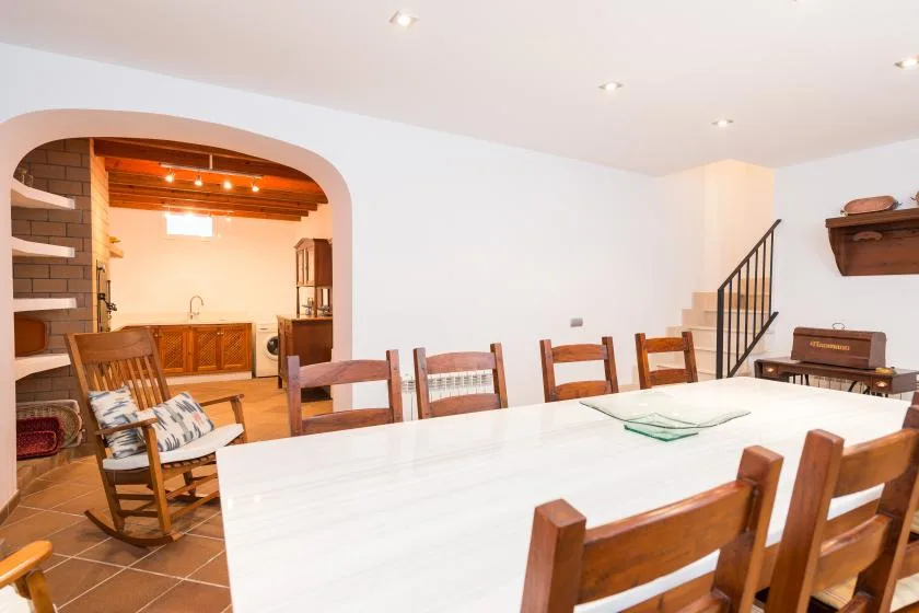 Comedor con una mesa larga y asientos de madera, abierto a una cocina.