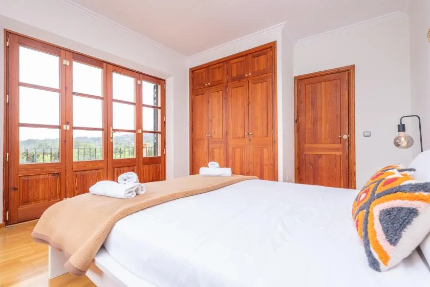 Un dormitorio con una cama junto a puertas de madera y grandes ventanas.