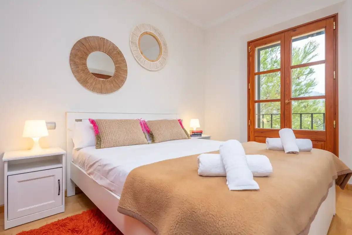 Un dormitorio luminoso con una cama hecha junto a una ventana con marco de madera.