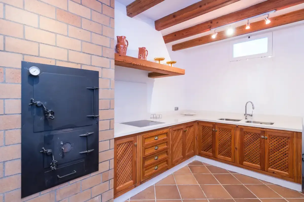 Una cocina rústica con armarios de madera y un horno negro empotrado en la pared de ladrillo.