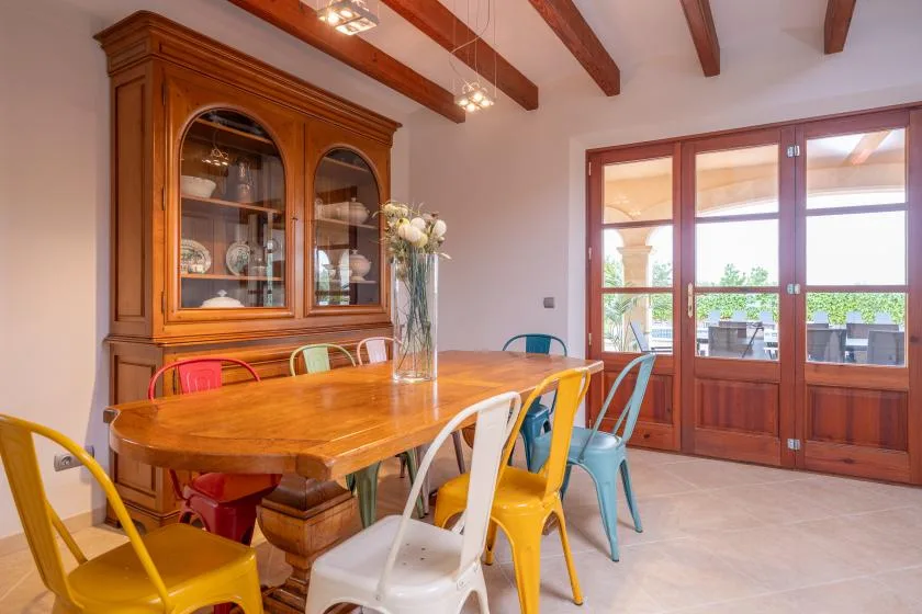 Un comedor con una mesa de madera, sillas de colores y puertas de vidrio.