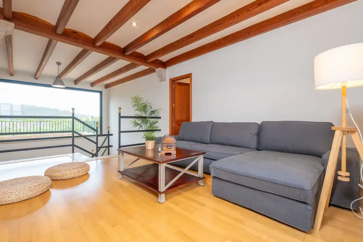 Una sala de estar con asientos grises, una mesa de centro y vigas de madera expuestas.