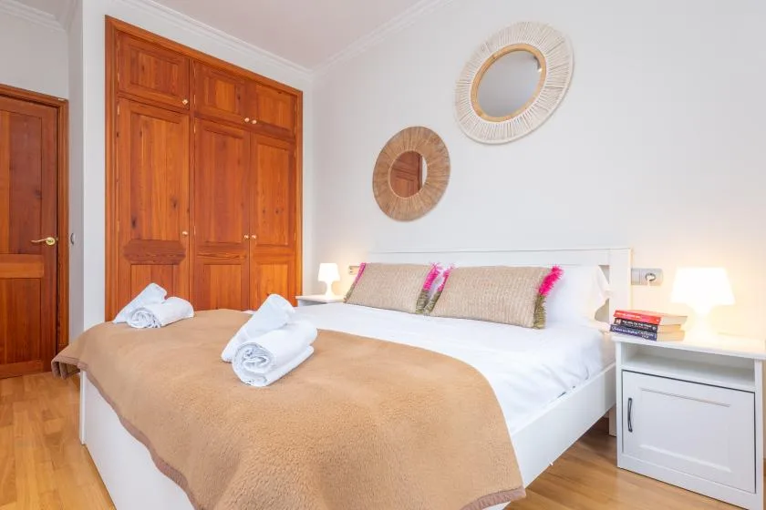 Un dormitorio con una cama blanca, una colcha beige y armarios de madera.