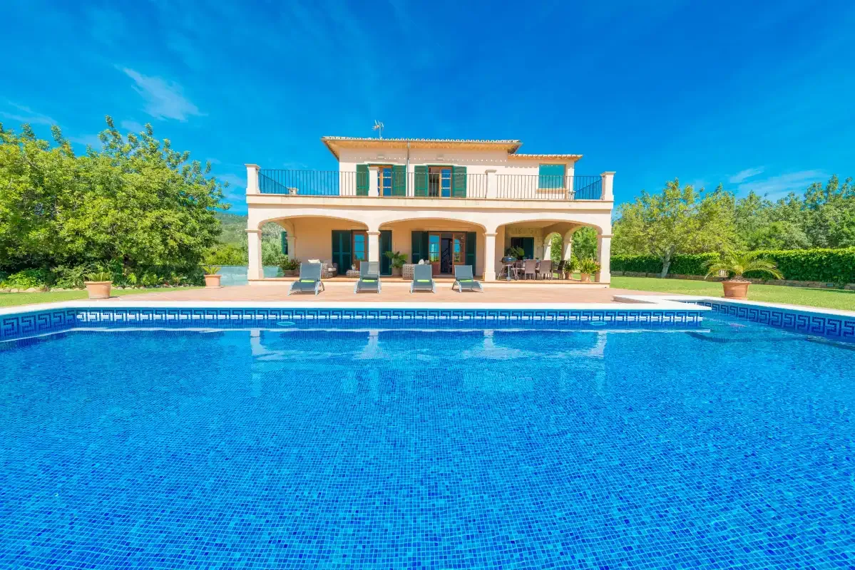 Una casa con terraza cubierta se encuentra detrás de una gran piscina.