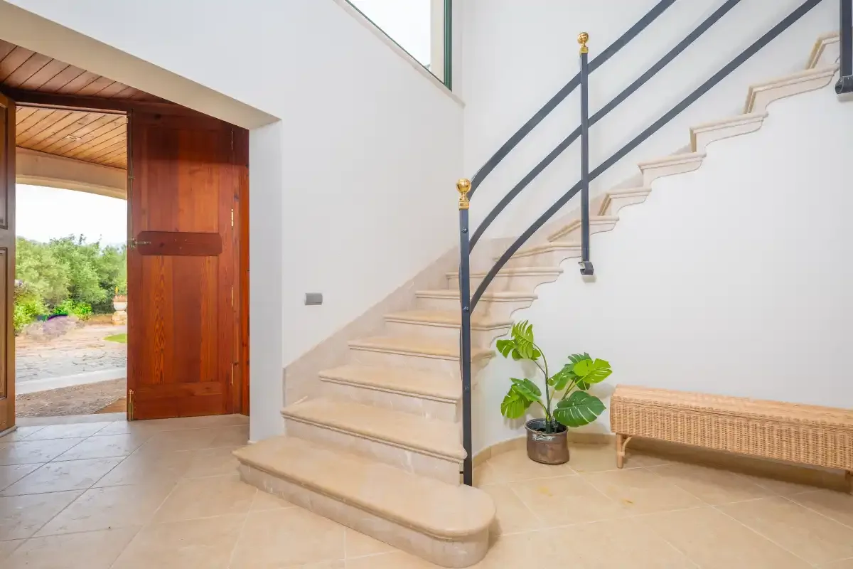Una entrada interior con una escalera y una puerta de madera abierta.