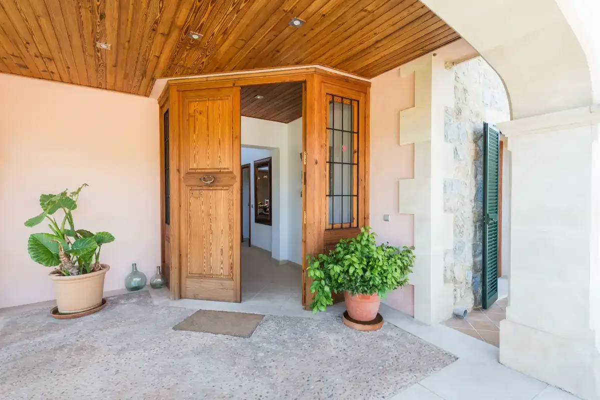 Un recibidor interior con una puerta de madera, plantas en macetas y un techo revestido de madera.