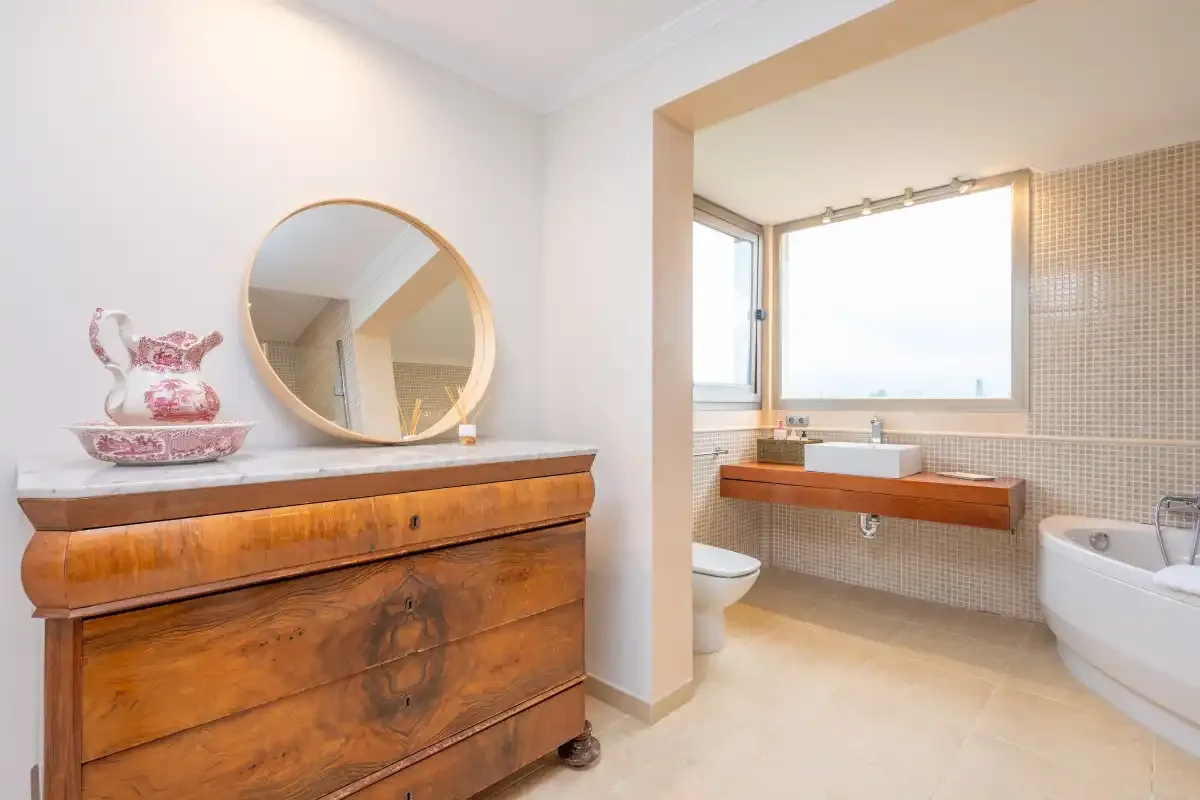 Un baño luminoso con un mueble de madera y una bañera junto a la ventana.