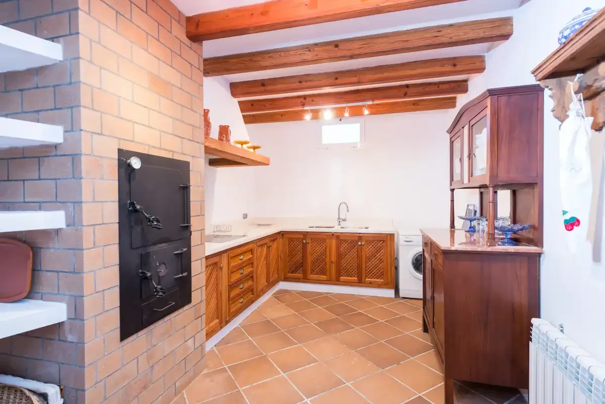 Una cocina con armarios de madera, suelo de baldosas y vigas de techo expuestas.