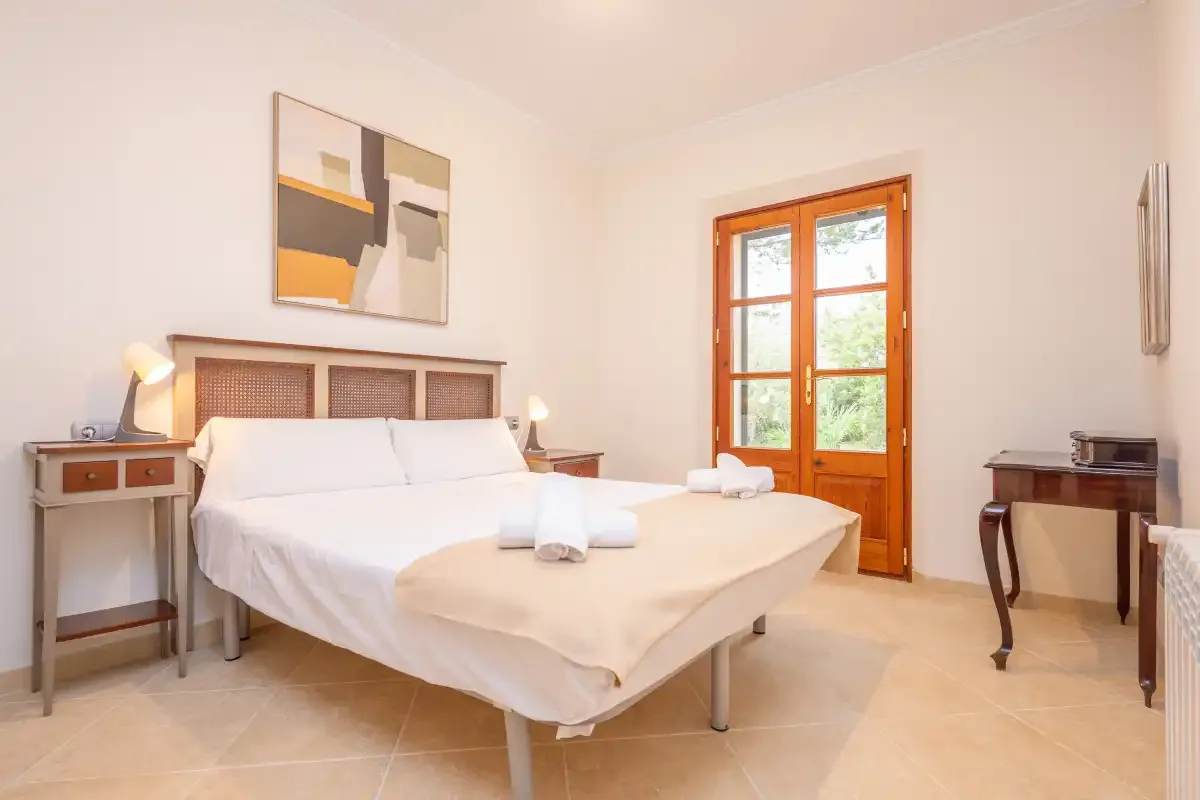 Un dormitorio luminoso con cama doble, mesillas y una puerta acristalada con marco de madera.