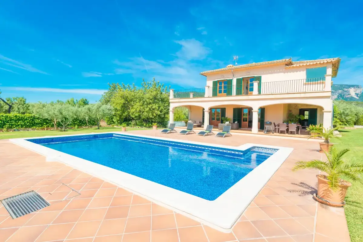 Una piscina y un patio de baldosas están frente a una casa de dos plantas.