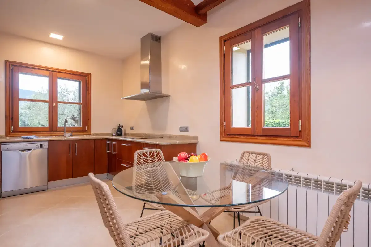 Comedor con una mesa de vidrio y asientos de mimbre junto a dos ventanas.