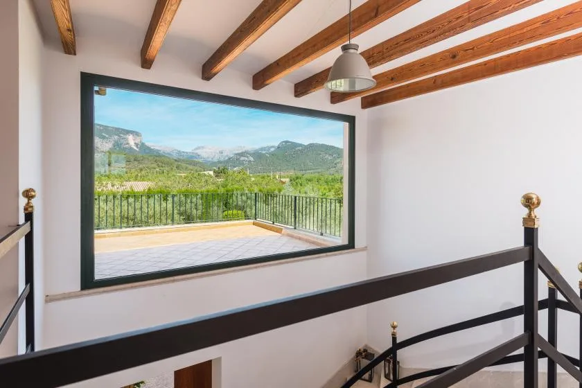 Una escalera se abre a una vista de montañas a través de una ventana grande.
