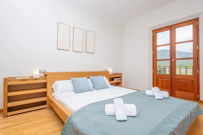 Un dormitorio luminoso con una cama tendida y puertas de vidrio con marco de madera.