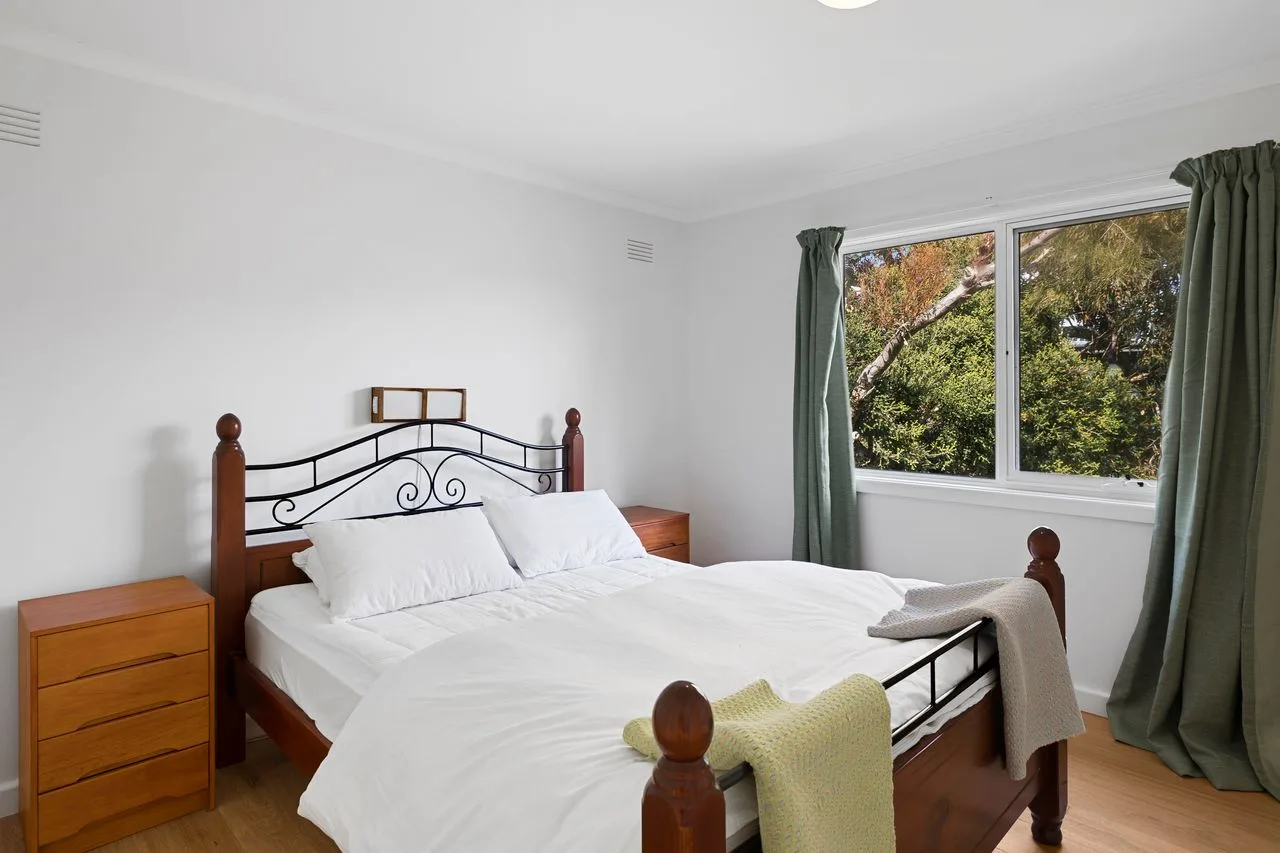 Un dormitorio luminoso con una cama tendida junto a una ventana grande.